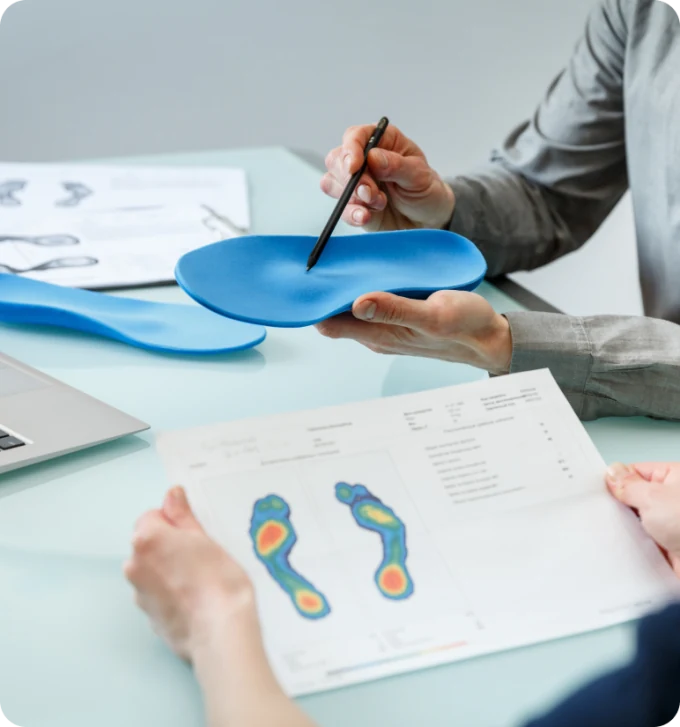 A clinician reviews a foot pressure scan beside a blue custom insole
